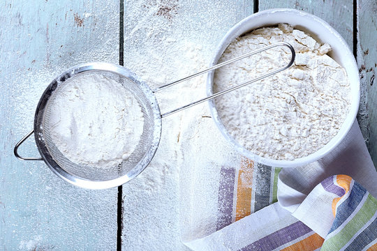 Sifting flour through sieve on wooden table, top view