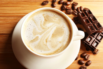 Cup of coffee latte art with grain and chocolate on wooden table, closeup