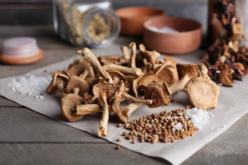 Dried mushrooms with spices on paper on wooden table, closeup