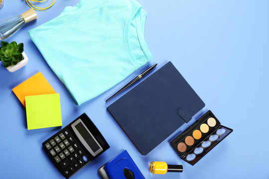Female shirt, cosmetics and office details on color table, top view