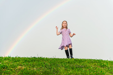Fototapeta na wymiar Little girl playing on the hill under the rainbow