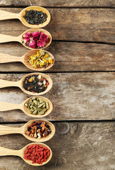 Collection of tea and natural additives in wooden spoons, on old wooden table