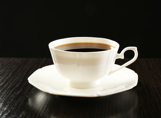 Cup of coffee on wooden table, on dark background