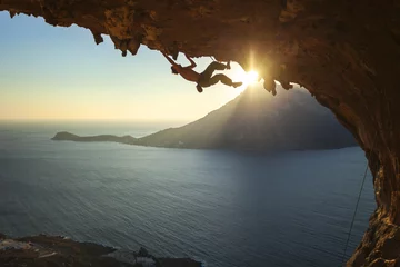 Gordijnen Male rock climber climbing along a roof in a cave at sunset  © Andrey Bandurenko