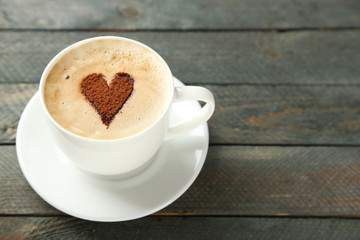 Cup of cappuccino with heart of cocoa on wooden table