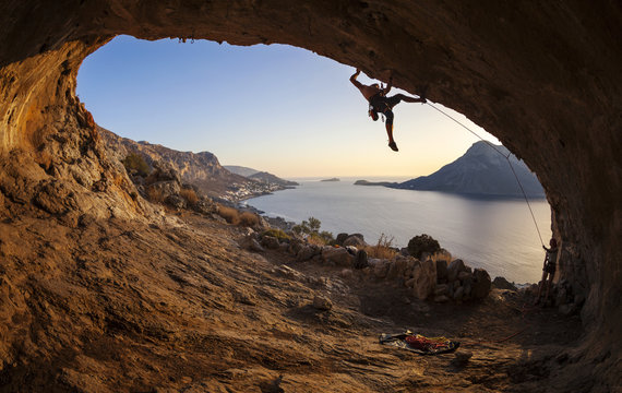 Male rock climber climbing along a roof in a cave at sunset 