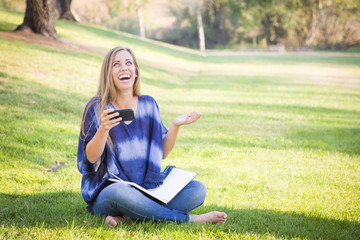 Laughing Young Woman with Book and Cell Phone Outdoors