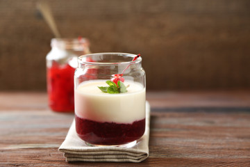Glass jar with tasty panna cotta dessert on plate, on wooden table