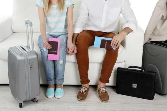 Legs of young happy couple with baggage and tickets, sitting on sofa