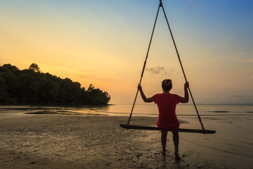 woman sit on swing bar look at sunset at the beach