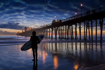 Admiration - silhouetted surfer at sunset near pier.