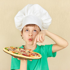 Young smiling kid in chefs hat with a cooked appetizing pizza