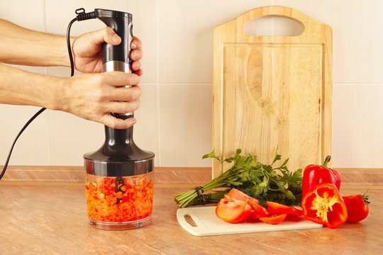 Hands cooks chopped red pepper in a blender