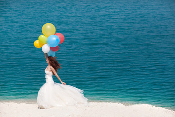 Young woman with balloons in white wedding dress on beach