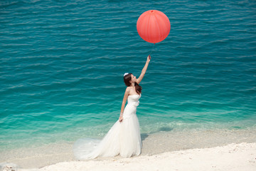 Woman with balloons in wedding dress on background of sea.