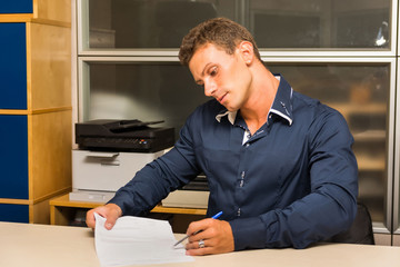 Young man doing paperwork at office desk, showing a document