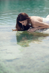 Woman lying in water and looking at the white wedding dress.