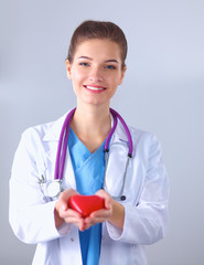 Young woman doctor holding a red heart, standing in hospital