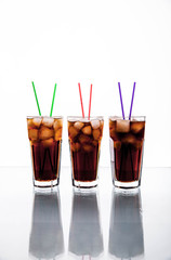 three glasses of cola with ice and straws on a white background.