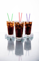 three glasses of cola with ice and straws on a white background.