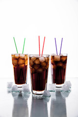 three glasses of cola with ice and straws on a white background.