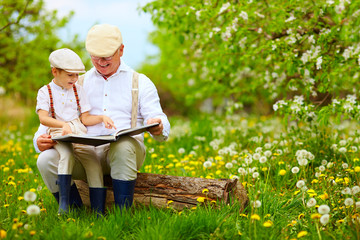 grandfather reading a book to his grandson, in blooming garden