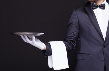 Waiter holding an empty silver tray against dark background