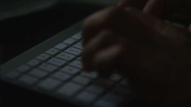 Male hands typing on a keyboard at night in slow motion
