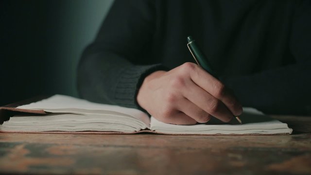 Young man sitting at desk and writing in a big notebook 