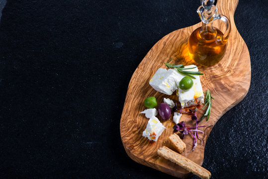Feta cheese on wooden board with olives and oil