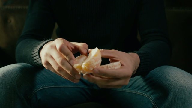 Young man sitting on a sofa and peeling an orange 