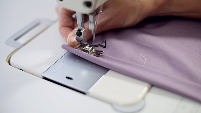 Female hands sewing on professional sewing machine.