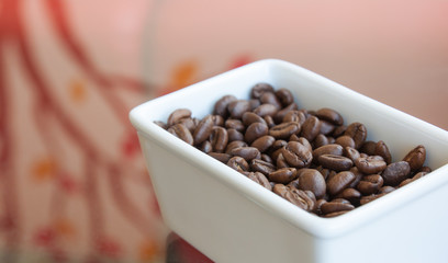 Coffee beans in a white cup on a glass table.