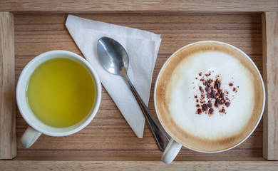 Cappuccino and hot green tea and a spoon on a wooden tray.