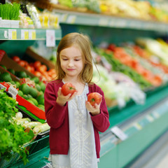 Little girl choosing tomatoes in a food store