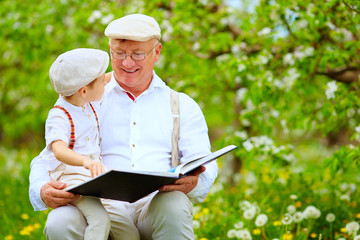 grandfather with grandson reading book in spring garden