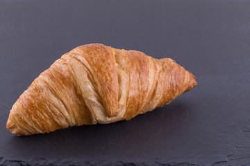 A Close up Image of a Croissant on a Slate Board.