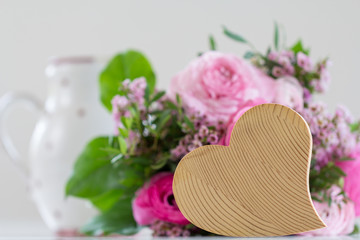 Ein hölzernes Herz vor einem Strauß rosa Rosen.