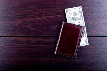 Maroon purse with hundred dollar bills on a burgundy table, top