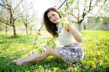 Naklejka na ściany i meble beautiful girl sitting under the flowering trees