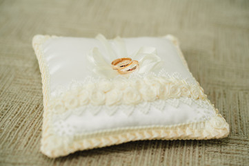 golden wedding rings on small white cushion