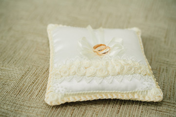 golden wedding rings on small white cushion