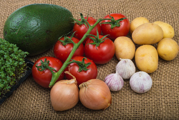 Avocada cress tomatoes onions garlic potatoes on rustic burlap