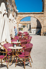 Stone arch in main square of Marzamemi and some chairs of a bar