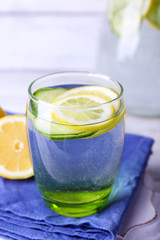 Fresh water with lemon and cucumber in glassware on wooden table, closeup