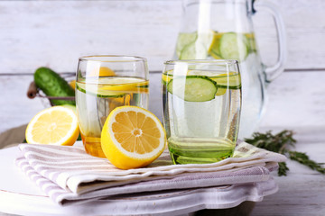 Fresh water with lemon and cucumber in glassware on wooden background