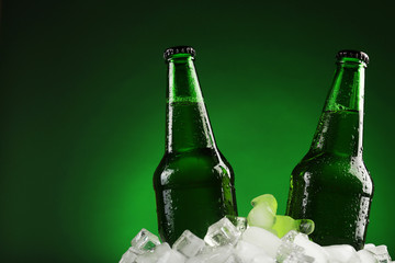 Glass bottles of beer in ice cubes on color background