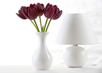 Beautiful violet tulip in vase with lamp on light background