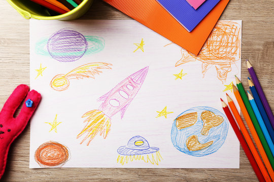 Kids drawing on white sheet of paper on wooden table, top view