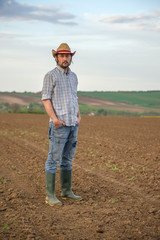 Naklejka na ściany i meble Male Farmer Standing on Fertile Agricultural Farm Land Soil
